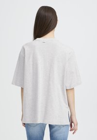 Pelēka pārmērīga izmēra T-krekls ar īsām piedurknēm un apaļu izgriezumu. Mīksts audums ar vienkāršu dizainu, dekorēts ar sānu šķēlumiem un nelielu logotipu aizmugurē.