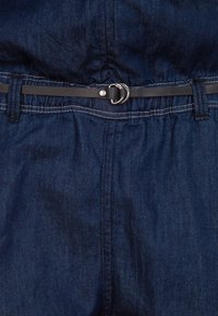 Mörkblå denimtyg med en slät yta. Har ett svart bälte med en silverfärgad spänne och sydda detaljer vid midjan.