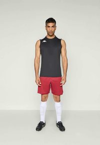 Svart ermeløs skjorte, røde shorts, hvite sokker, svarte fotballsko. Kappa-logo på skjorten; tettsittende atletisk design. Enkelt og glatt tekstur.