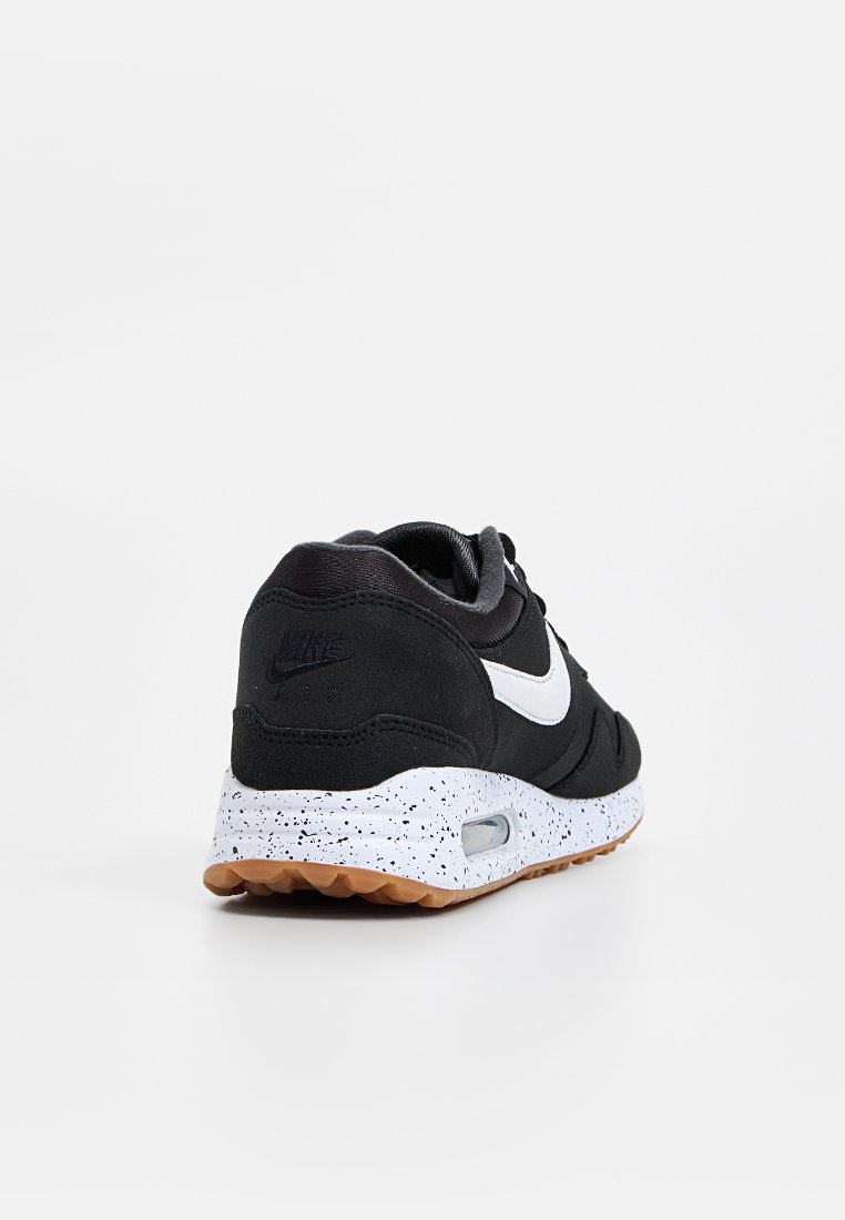 Zwarte sneaker met een bovenwerk van suede en textiel, witte swooshlogo, gespikkelde witte tussenzool en een bruine rubberen buitenzool. Voorzien van luchtkussens.