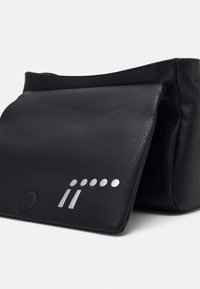 Musta nahkalaukku, jossa on taittuva läppä, sileä pinta ja hopea yksityiskohta. Etupuolella on pyöreä yksityiskohta ja kaksi hopeista viivaa.