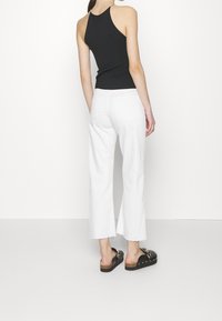 Schwarzes Halftertop, weiße weite Jeans und klobige schwarze Sandalen mit goldenen Akzenten. Glatter Stoff mit einer figurbetonten Silhouette.