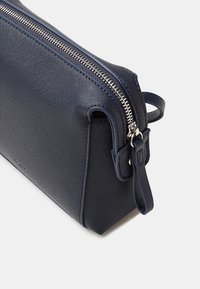 Tracolla in pelle blu navy a trama con zip argentata e linguetta in pelle su sfondo bianco.