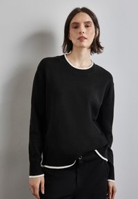 Svart tröja med ribbad halsringning och nederkant, med vita detaljer vid kragen och ärmsluten. Mjuk textur, lös passform.