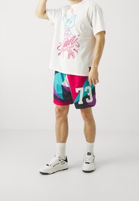 Camiseta de algodón blanca con estampado gráfico en azul y rosa; pantalones cortos de patrón geométrico multicolor; zapatillas blancas con detalles en negro.