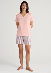 Top rosa chiaro con maniche corte e scollo a V abbinato a pantaloni corti a righe rosa e bianche, con linee verticali e una texture di tessuto morbida e traspirante.