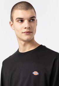 Zwarte lange mouw t-shirt van katoen. Heeft een klein, kleurrijk Dickies-logo op de borst. Ronde halslijn en een zachte textuur.