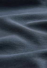 Tessuto in velluto blu scuro con una sottile trama a coste, che mostra onde morbide e fluide e una finitura superficiale liscia.