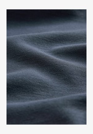 Tissu texturé bleu foncé avec un motif côtelé subtil, affichant des vagues douces et fluides ainsi qu'une finition de surface lisse.