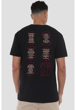 Black cotton t-shirt featuring bold red text on the back with numbered titles and references, short sleeves, and a relaxed fit.