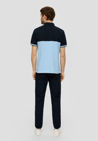 Koszulka polo w granatowej górnej części i jasnoniebieskim dolnym segmencie, z klasycznym kołnierzykiem i kontrastowym wykończeniem, w połączeniu z granatowymi spodniami.