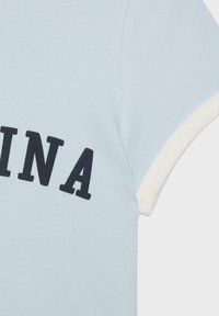 Chemise bleu clair à manches courtes avec bordure blanche sur la manche et grandes lettres noires "INA" imprimées à l'avant.