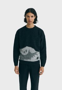 Maglione nero a maglia con un motivo di montagna grigia, caratterizzato da un collo e orlo a coste. Texture morbida con una vestibilità rilassata.
