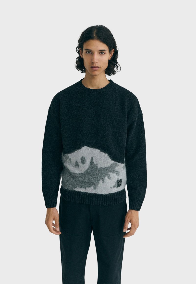 Maglione nero a maglia con un motivo di montagna grigia, caratterizzato da un collo e orlo a coste. Texture morbida con una vestibilità rilassata.