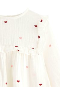 Weißes Baumwollkleid mit gestickten Herzen in Rot und Pink, einem Rüschenausschnitt und langen Ärmeln. Strukturierter Stoff mit zarten Details.