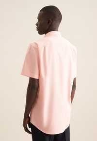 Camicia a maniche corte di colore rosa chiaro, con colletto moderno. Presenta un orlo dritto e una texture sottile, evidenziando una vestibilità su misura dal retro.