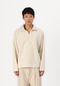 Lys beige fleece-pullover med en blød, struktureret overflade, der har krave og sænkede skuldersømme.