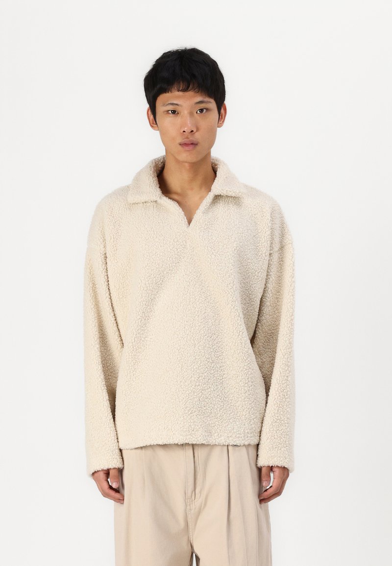 Lys beige fleece-pullover med en blød, struktureret overflade, der har krave og sænkede skuldersømme.