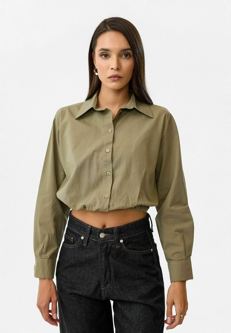 Olijfgroene cropped shirt met een klassieke kraag, knopen aan de voorkant en pofmouwen. Gecombineerd met hoge taille donkere denim jeans.