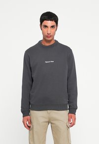 Sweat-shirt en coton gris avec col et poignets côtelés, orné d'un texte brodé blanc sur la poitrine, associé à un pantalon cargo beige clair.