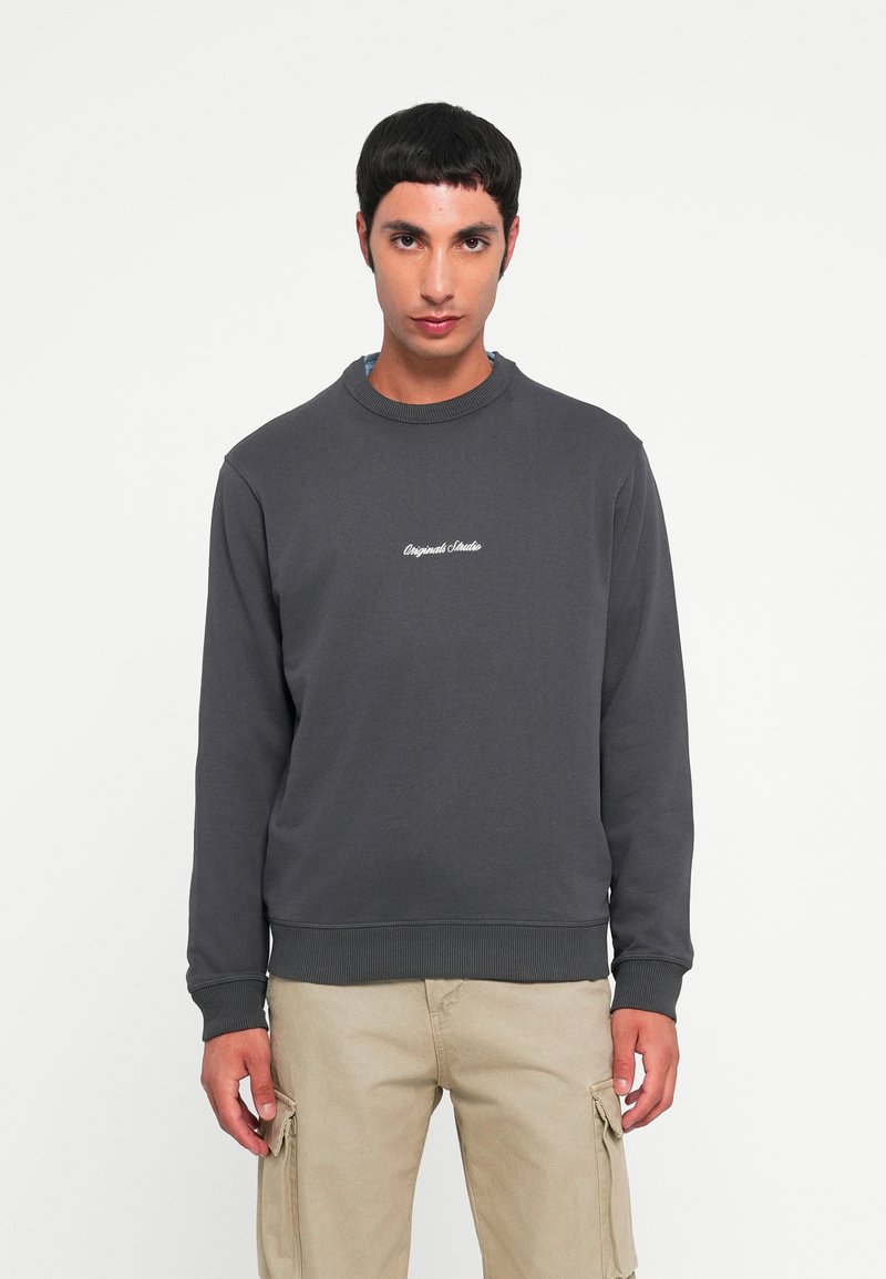 Sweat-shirt en coton gris avec col et poignets côtelés, orné d'un texte brodé blanc sur la poitrine, associé à un pantalon cargo beige clair.