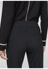 Black athletic pants with a relaxed fit and elastic waistband. Smooth texture with a subtle sheen and a single back pocket detail.