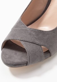 Šedé sukně otevřené boty s designem křížového pásku, hladkým vnitřním podšíváním a malým podpatkem. Texturovaný povrch zvyšuje přilnavost.