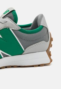 Zapatilla gris con acentos verdes, que presenta una parte superior texturizada, un cuello acolchado, una entresuela blanca y una suela exterior de goma con un patrón de dibujo.