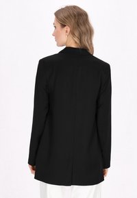 Černý elegantní blejzr s dlouh�ými rukávy, jednoduchým límečkem a středovým švem na zadní straně. Design má hladkou strukturu a čisté linie.