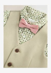 Hellbeige Weste mit zwei braunen Knöpfen, kombiniert mit einem grün-weißen gemusterten Hemd und einer pinken Fliege.