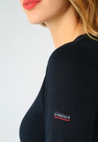 Granatowa prążkowana bluzka z długim rękawem z okrągłym dekoltem i małą czerwoną i białą metką "Armor Lux" na lewym rękawie.