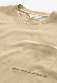 Beige afslappet T-shirt lavet af bomuld, med rund halsudskæring og en lomme på venstre bryst med en glat tekstur.