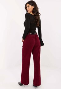 Bordowe szerokie spodnie sztruksowe o fakturowanym wykończeniu, z czarnym paskiem w talii i bocznymi kieszeniami. Zaprezentowane wraz z dopasowanym czarnym topem.