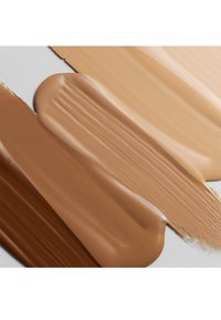 Trois échantillons de fond de teint liquide : brun foncé, beige moyen et beige clair. Texture lisse avec une finition brillante ; saturation de couleur uniforme.