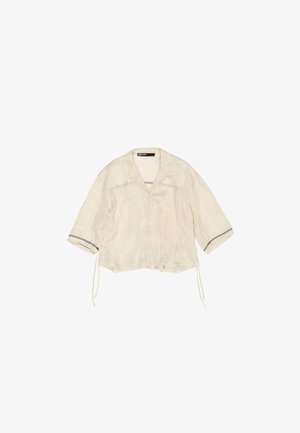 Blusa bianca sporca con colletto, maniche a tre quarti, chiusura con bottoni e tessuto testurizzato. Presenta dettagli neri sui orli delle maniche.