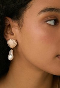 Orecchini dorati con design a conchiglia e un accento di perla a forma di goccia bianca. Superficie liscia con una leggera lucentezza.