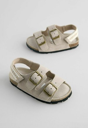 Beige Wildledersandalen mit zwei verstellbaren Riemen, goldfarbenen Schnallen und einer strukturierten Sohle. Akzentuiert mit geflochtenen Details und Logo.