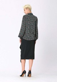 Blouse florale vert foncé avec des manches ballon, portée avec une jupe crayon noire jusqu'au genou et des escarpins noirs.