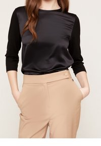 Svart och satäng långärmad topp med en kontrasterande svart liv; i kombination med beige skräddarsydda byxor med sidfickor och en knappdetalj.