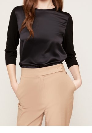 Black and satin long-sleeve top with a contrasting black bodice; paired with beige tailored pants featuring side pockets and a button accent.
