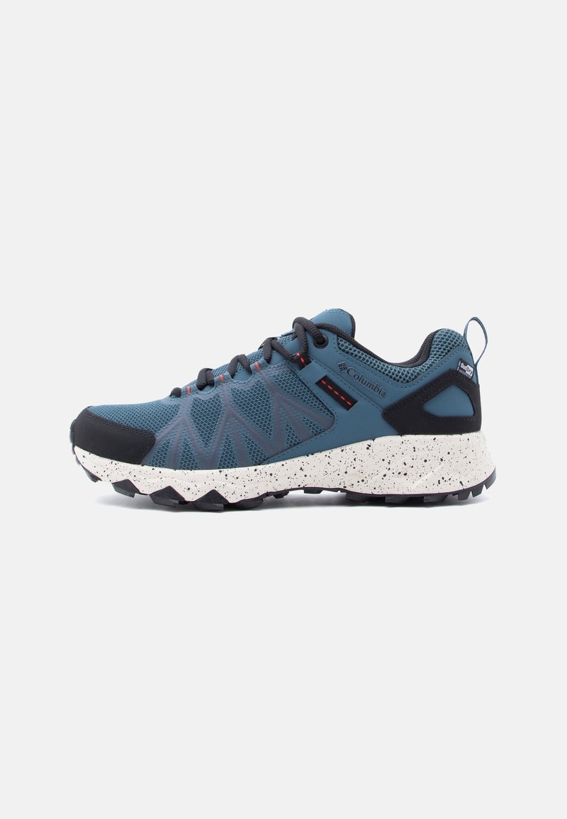 Chaussure de trail Columbia bleue et noire avec semelle blanche mouchetée, tige en mesh et languette au talon, vue de côté sur fond blanc.