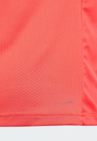 Élénk korall színű sportmez, nedvességelvezető anyagból készült, texturált felülettel, mikro-perforációkkal, és a hemnél található "ClimaCool" márkázással.