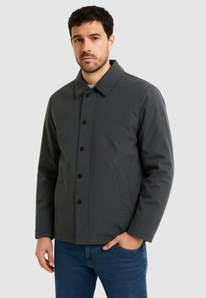 Giacca grigia impermeabile con chiusura a bottoni, collo sagomato e tasche laterali. Tessuto liscio con design minimalista e dettaglio con logo sulla manica.