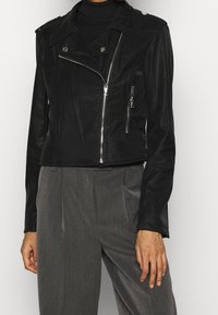 Giacca cropped in finta pelle nera con zip frontale, tasche con zip e spalline; presenta un motivo texturizzato lungo l'orlo.