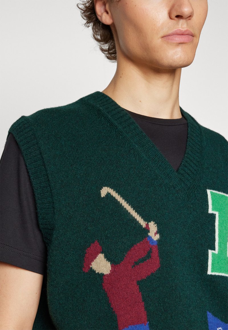 Gilet verde lavorato a maglia con scollatura a V, caratterizzato da un design colorato di un golfista in rosso e blu. Tessuto testurizzato con bordi a coste e vestibilità sagomata.