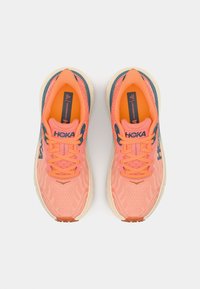 Hoka running shoes featuring a breathable coral mesh upper, orange laces, and beige sole with textured patterns and logo accents.