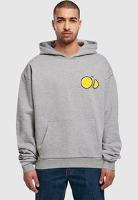 Hoodie i lys grå med en frontlomme og et citrongrafik på brystet. Lavet af blødt stof med en afslappet pasform.