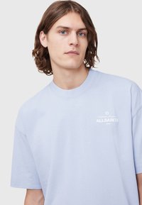 Light blue cotton T-shirt with short sleeves, featuring a crew neckline and the "ALLSAINTS" logo printed in white on the chest.
