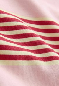 Tissu doux avec des rayures horizontales rouges et crème sur un fond rose pâle, montrant la texture et de légers plis.