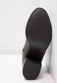 Grijze suède enkellaars met een gestructureerde zwarte rubberen zool, voorzien van een gladde afwerking en een minimalistisch ontwerp. Accenten zijn onder andere gestikte details.